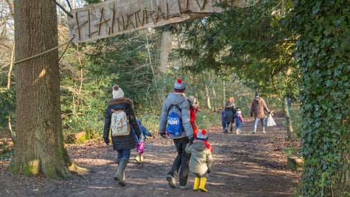 Families in winter clothes and wellies, walking along the path to the natural play area at Box Hill